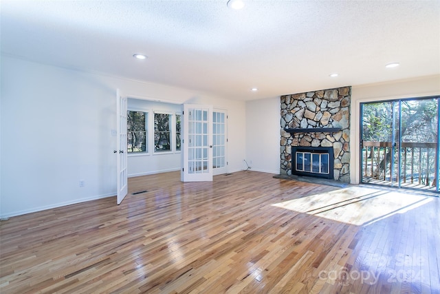 unfurnished living room featuring french doors, a textured ceiling, hardwood / wood-style flooring, and a stone fireplace