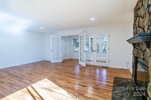 unfurnished living room with hardwood / wood-style flooring, a stone fireplace, and french doors