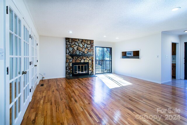 unfurnished living room featuring hardwood / wood-style flooring, a stone fireplace, a textured ceiling, and french doors