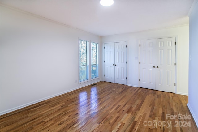 unfurnished bedroom with wood-type flooring, crown molding, and multiple closets