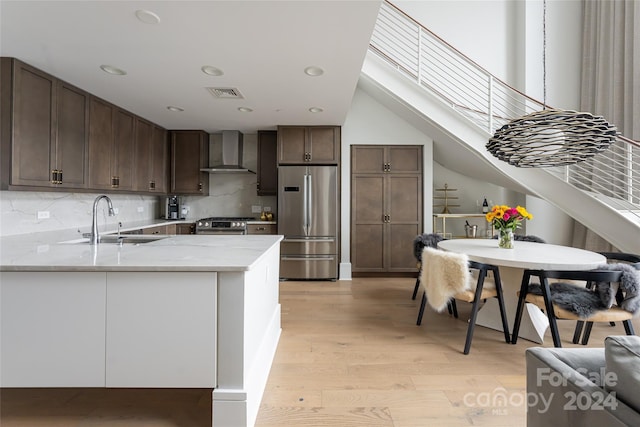 kitchen featuring sink, wall chimney exhaust hood, appliances with stainless steel finishes, light hardwood / wood-style floors, and kitchen peninsula