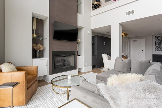 living room featuring a fireplace, light wood-type flooring, and a towering ceiling