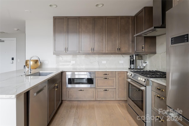 kitchen with stainless steel appliances, wall chimney range hood, tasteful backsplash, kitchen peninsula, and light wood-type flooring