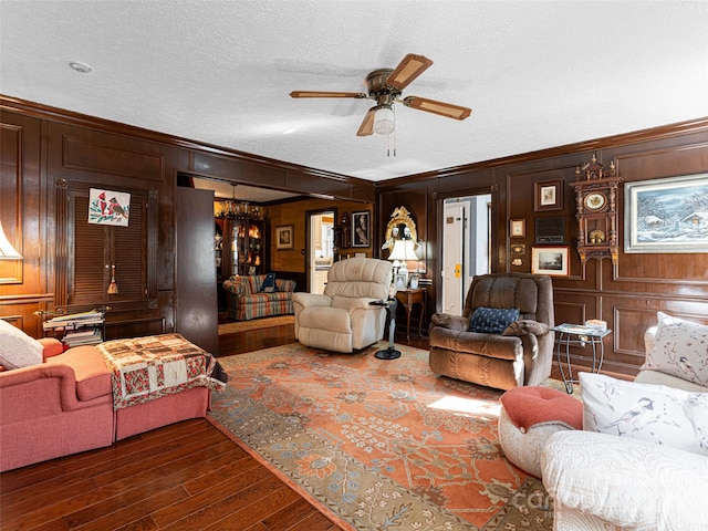 living room with wood walls, ceiling fan with notable chandelier, ornamental molding, a textured ceiling, and dark hardwood / wood-style flooring