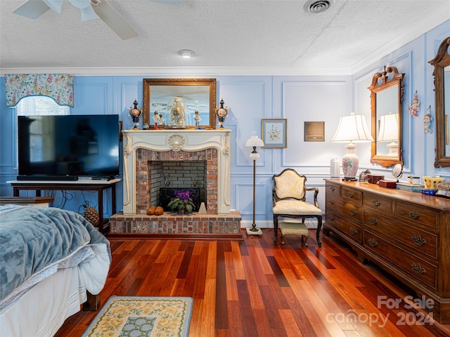 bedroom with a textured ceiling, ceiling fan, dark wood-type flooring, and a brick fireplace