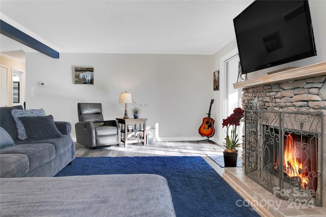 living room with beam ceiling, a stone fireplace, and light hardwood / wood-style flooring