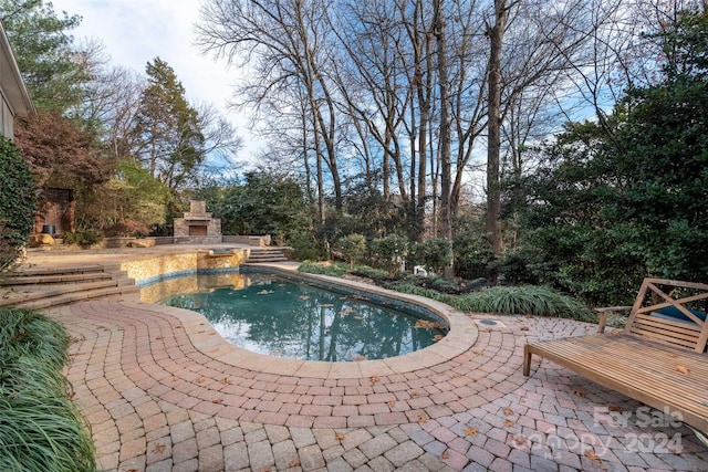 view of pool featuring an outdoor stone fireplace and a patio