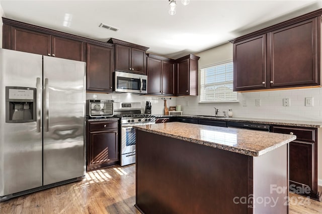 kitchen with a center island, light wood-type flooring, appliances with stainless steel finishes, tasteful backsplash, and light stone counters