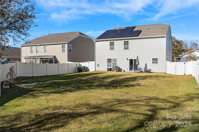 back of property with solar panels and a yard