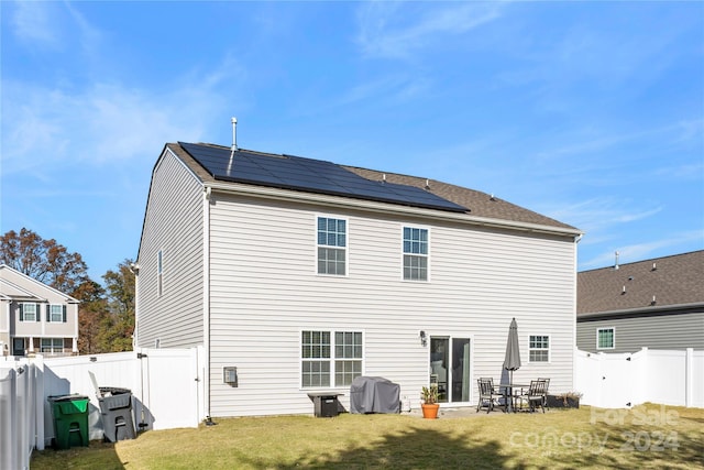 rear view of house featuring solar panels and a yard