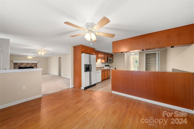 kitchen with kitchen peninsula, white appliances, ceiling fan, a fireplace, and light hardwood / wood-style floors