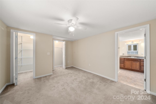 unfurnished bedroom with ensuite bath, ceiling fan, a walk in closet, light carpet, and a closet