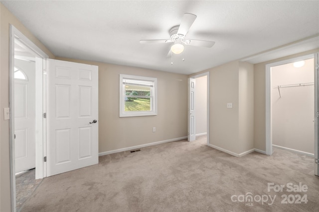 unfurnished bedroom featuring ceiling fan, light colored carpet, a walk in closet, and a closet