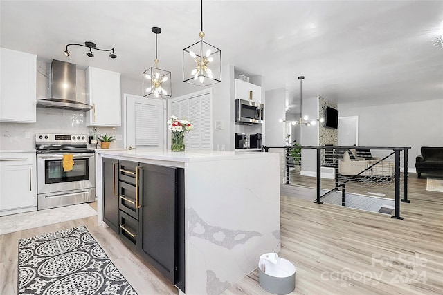 kitchen featuring white cabinetry, wall chimney exhaust hood, light hardwood / wood-style flooring, pendant lighting, and appliances with stainless steel finishes