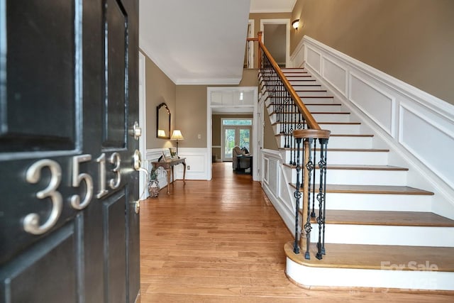 entrance foyer featuring a wainscoted wall, a decorative wall, stairway, ornamental molding, and wood finished floors