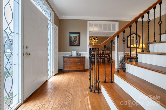 foyer with a wainscoted wall, crown molding, stairway, light wood-style flooring, and an inviting chandelier