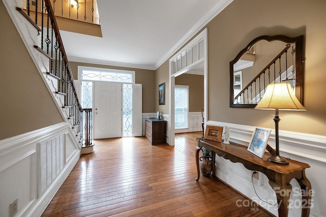 foyer entrance with a wainscoted wall, stairway, wood finished floors, and ornamental molding