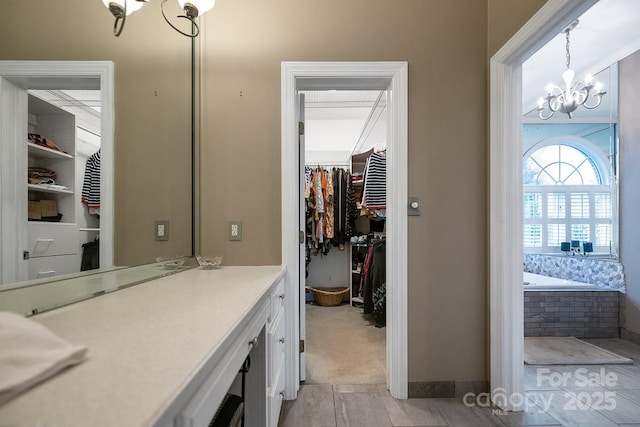 bathroom featuring a garden tub, a spacious closet, a chandelier, and vanity