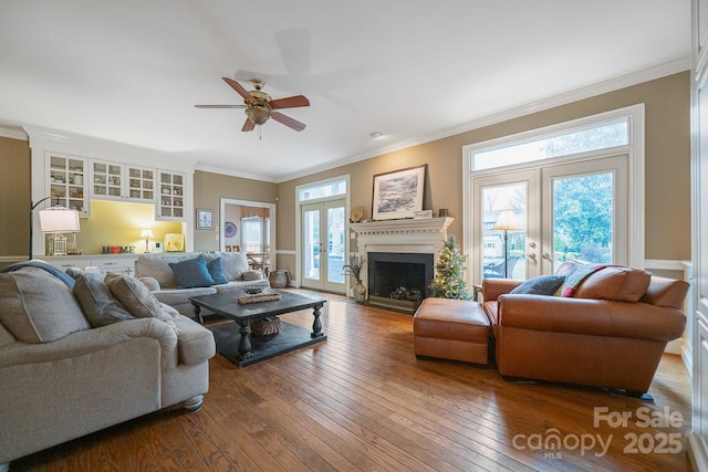 living area featuring a fireplace, wood finished floors, a ceiling fan, french doors, and crown molding