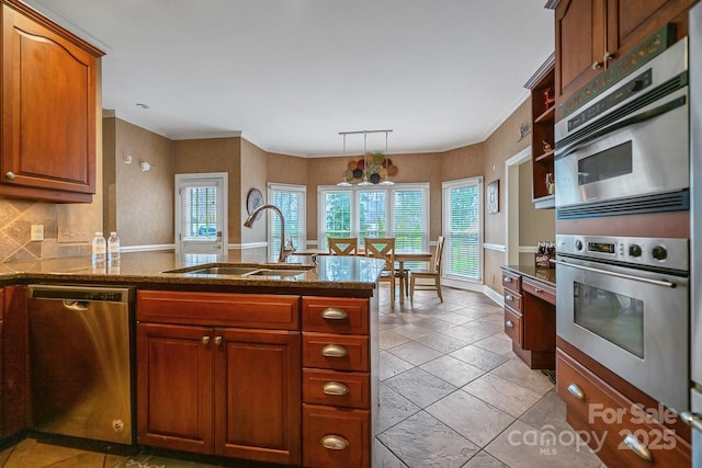 kitchen featuring dark stone counters, appliances with stainless steel finishes, hanging light fixtures, a peninsula, and a sink