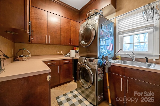 washroom with ornamental molding, stacked washing maching and dryer, a sink, and cabinet space