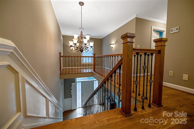 stairs with an inviting chandelier, crown molding, baseboards, and wood finished floors