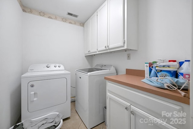 clothes washing area with light tile patterned flooring, cabinet space, washing machine and dryer, and visible vents