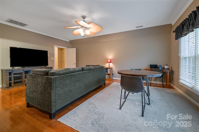 living room with ornamental molding, dark wood-style flooring, visible vents, and baseboards