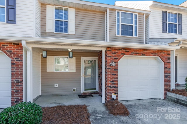 doorway to property featuring a garage, concrete driveway, and brick siding