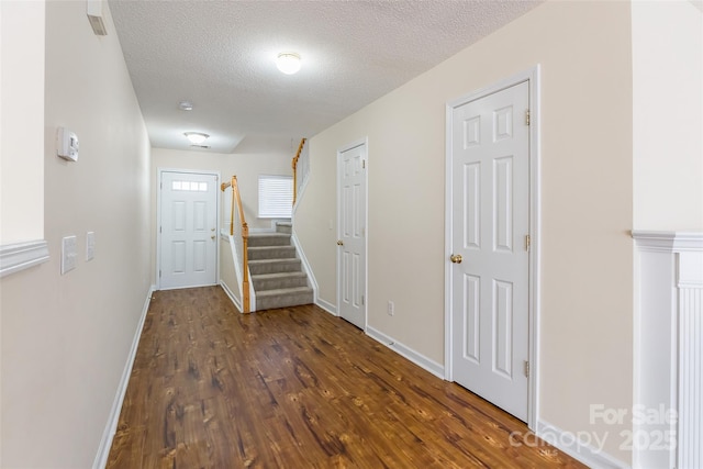 hallway featuring a textured ceiling, dark wood-style flooring, stairway, and baseboards