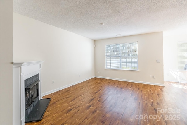 unfurnished living room with a fireplace with raised hearth, a textured ceiling, wood finished floors, and baseboards