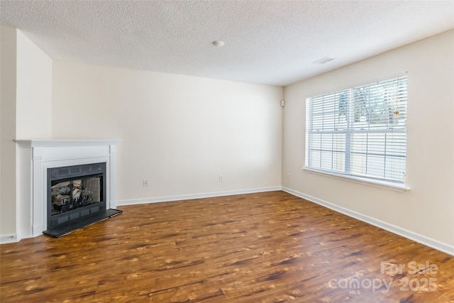 unfurnished living room featuring a textured ceiling, baseboards, a fireplace with raised hearth, and wood finished floors