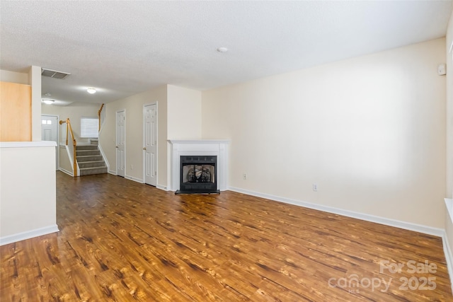 unfurnished living room with baseboards, visible vents, stairway, wood finished floors, and a fireplace