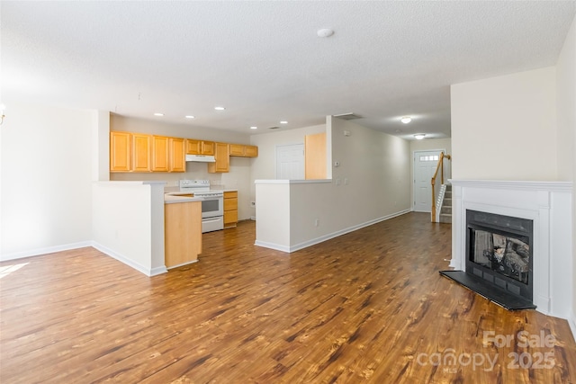 kitchen featuring open floor plan, wood finished floors, a peninsula, under cabinet range hood, and white range with electric cooktop