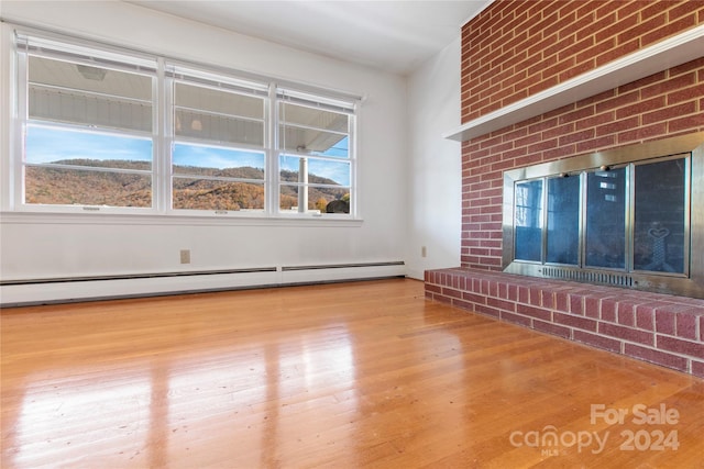 unfurnished living room featuring a healthy amount of sunlight, light wood-type flooring, a fireplace, and a baseboard radiator