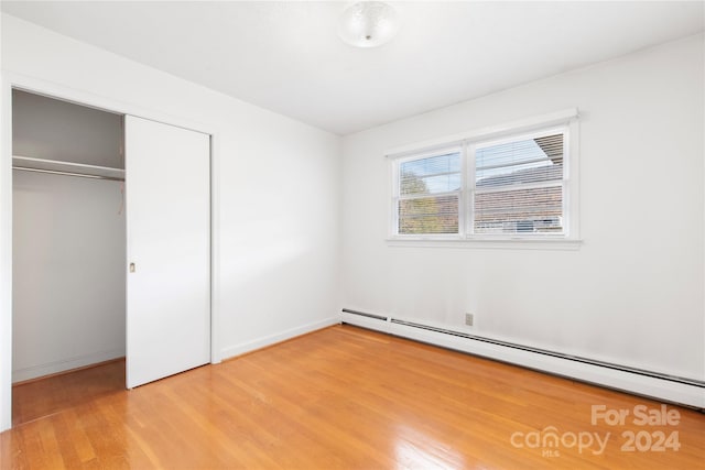 unfurnished bedroom featuring a closet, hardwood / wood-style flooring, and baseboard heating