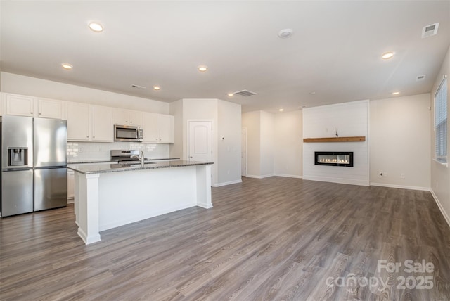 kitchen featuring light stone countertops, a large fireplace, stainless steel appliances, a center island with sink, and white cabinetry