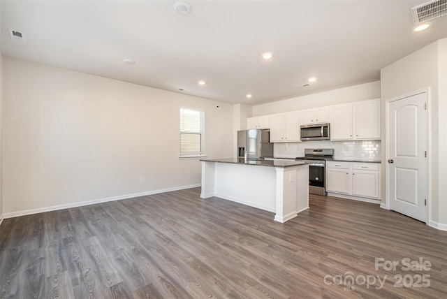 kitchen with backsplash, a kitchen island with sink, white cabinets, dark hardwood / wood-style flooring, and stainless steel appliances