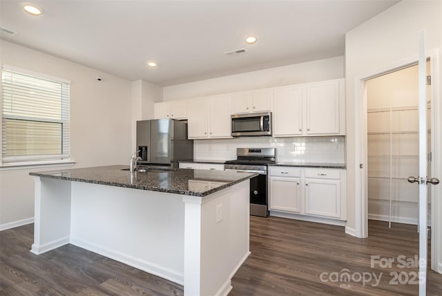 kitchen with dark wood-type flooring, dark stone countertops, a center island with sink, white cabinets, and appliances with stainless steel finishes