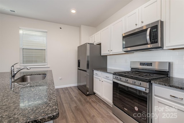 kitchen with white cabinets, stainless steel appliances, dark stone counters, and sink