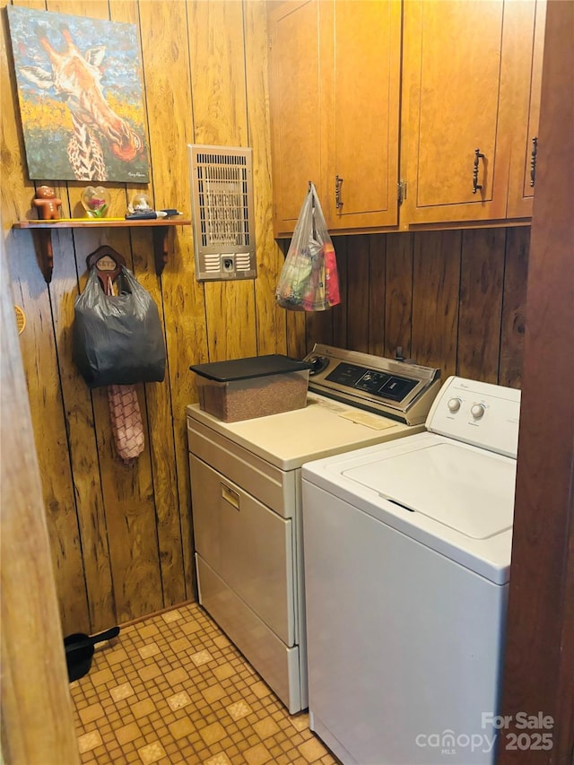 laundry area featuring heating unit, wooden walls, washer and clothes dryer, and cabinets