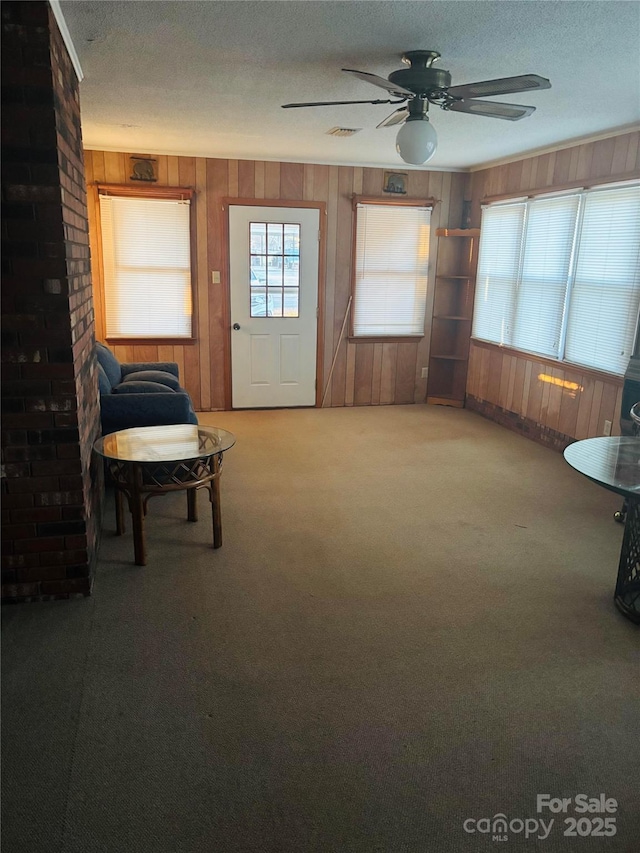 unfurnished room with wooden walls, carpet, ceiling fan, and a textured ceiling