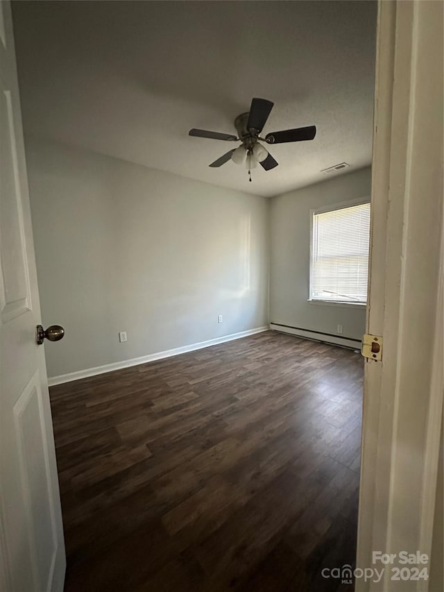 empty room featuring baseboard heating, ceiling fan, and dark hardwood / wood-style floors