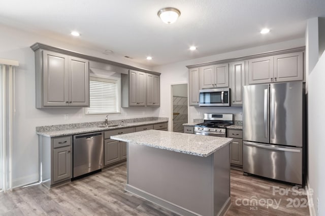 kitchen with light stone counters, stainless steel appliances, wood-type flooring, gray cabinets, and a kitchen island