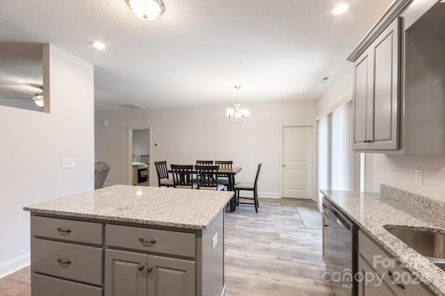 kitchen with gray cabinetry, ceiling fan with notable chandelier, stainless steel dishwasher, light wood-type flooring, and light stone counters