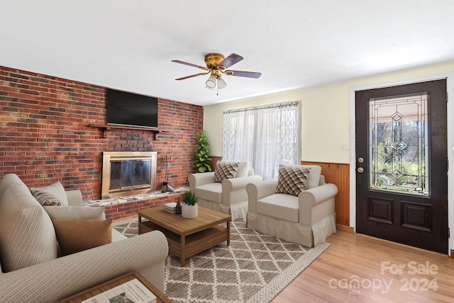 living room with ceiling fan, wood walls, a fireplace, and light hardwood / wood-style flooring