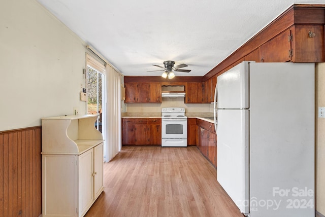 kitchen with white appliances, wooden walls, ceiling fan, light wood-type flooring, and range hood