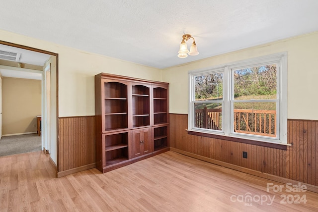 empty room featuring wooden walls, a notable chandelier, a textured ceiling, and light wood-type flooring