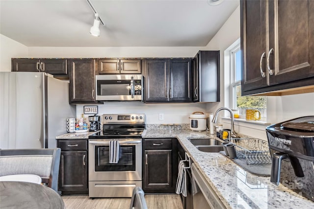 kitchen featuring sink, light hardwood / wood-style flooring, light stone countertops, dark brown cabinets, and stainless steel appliances