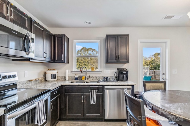 kitchen with light stone countertops, dark brown cabinetry, stainless steel appliances, sink, and light hardwood / wood-style flooring